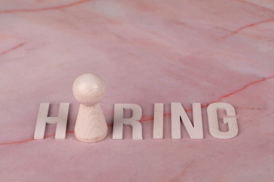 Drvena slova koja formiraju riječ 'hiring' na roza mramornoj podlozi.